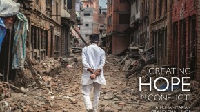 A man walks through a neighborhood surrounded by rubble with his hands crossed behind his back